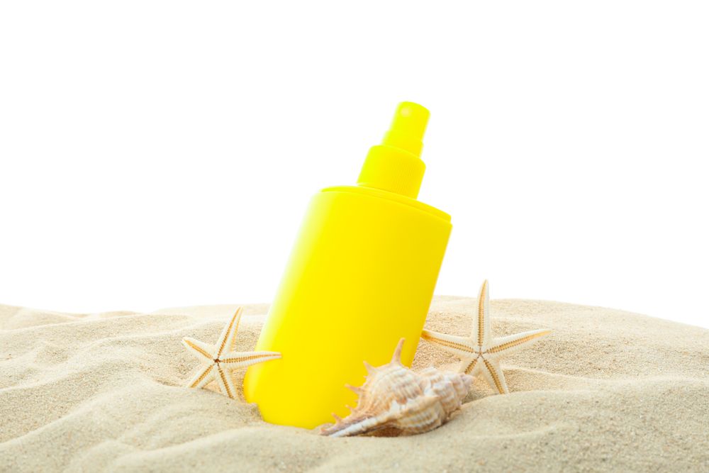 Sunscreen with starfish and seashells on clear sea sand isolated on plain background. Summer vacation