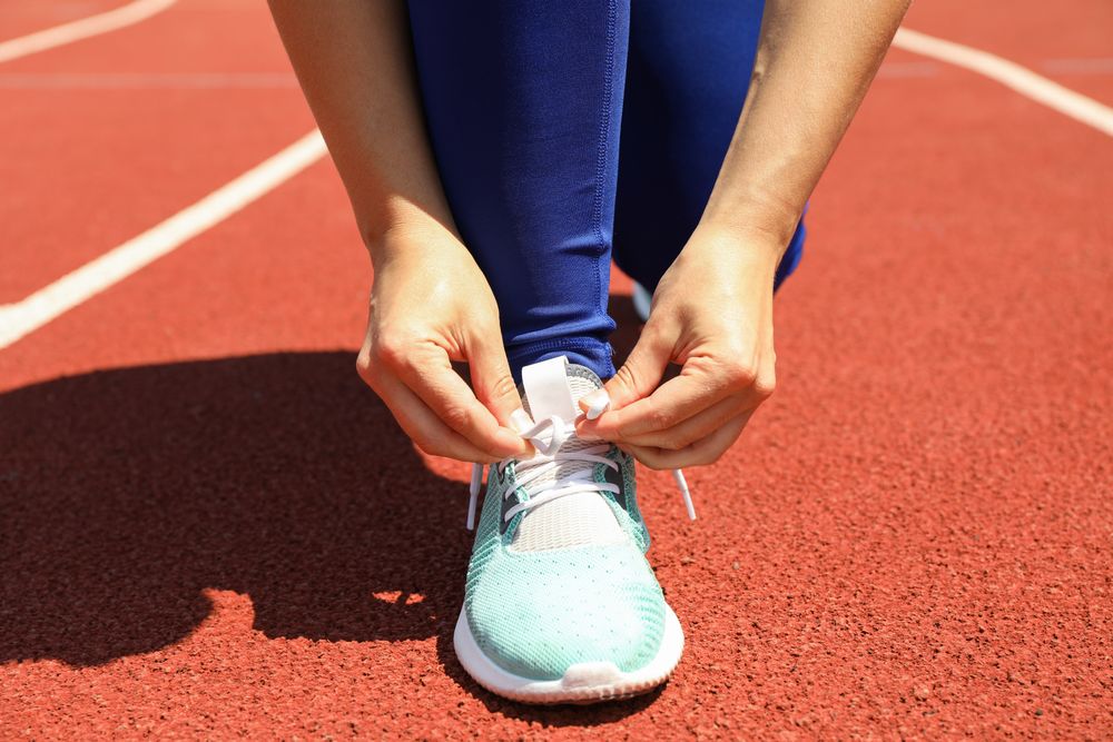 Girl tying shoelaces on red athletic running track, close up