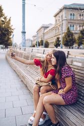 Laughing women taking selfie on wooden bench at street