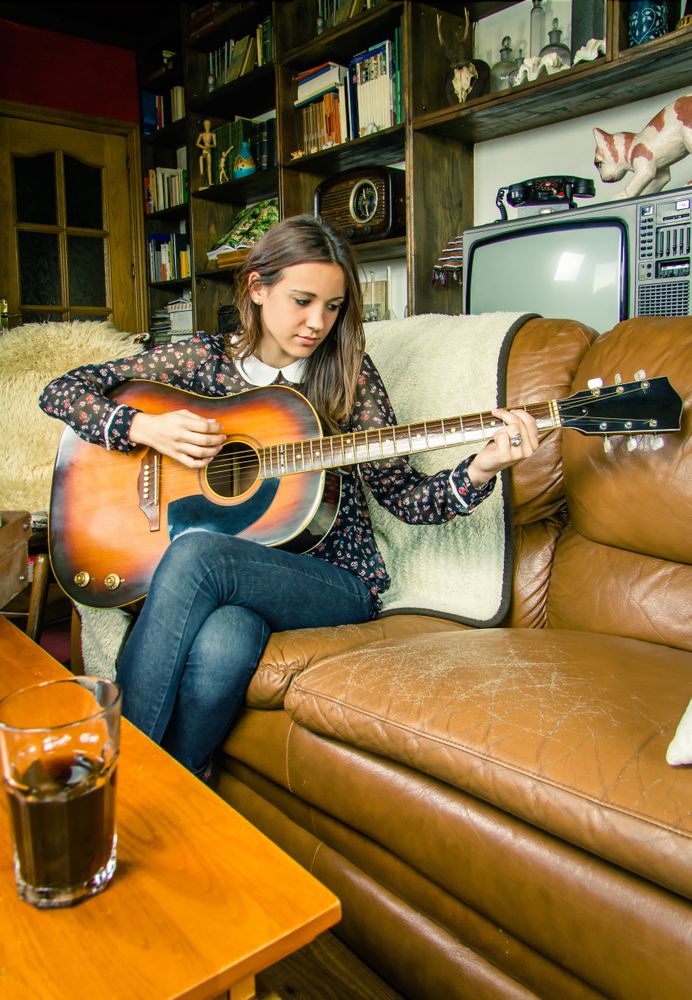 Young hipster woman playing acoustic guitar at home