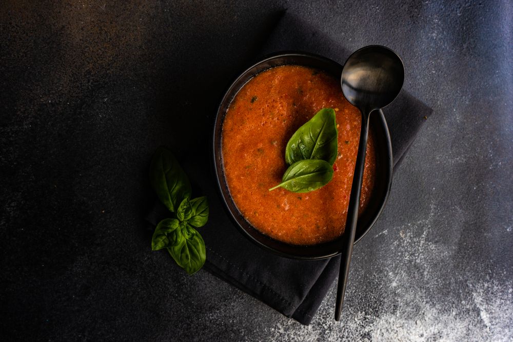 Dark bowl of gazpacho soup with basil leaves