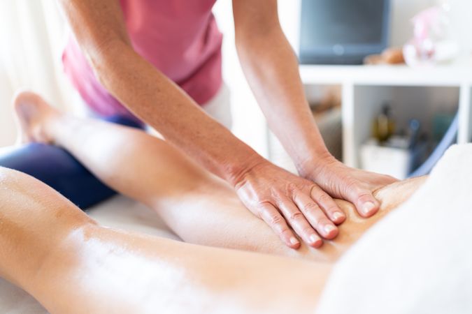 Crop masseuse rubbing oily skin of client during body massage in clinic