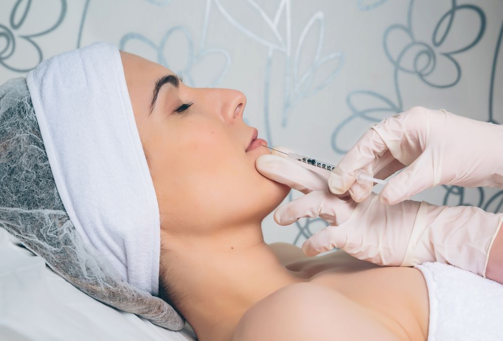Side view of aesthetician's hand's in latex gloves injecting botox into female's lips in a beauty salon