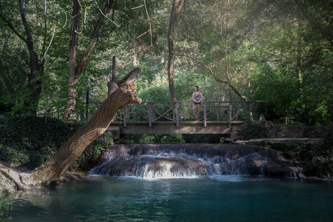 Woman standing on bridge above creek in forest
