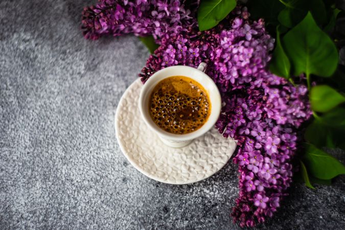 Pink lilac flowers surrounding cup of espresso