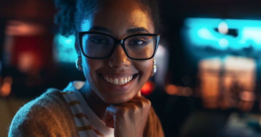 Close Up Portrait of a Young Black Woman with Glasses, Looking at Camera, Smiling in a Creative Office.