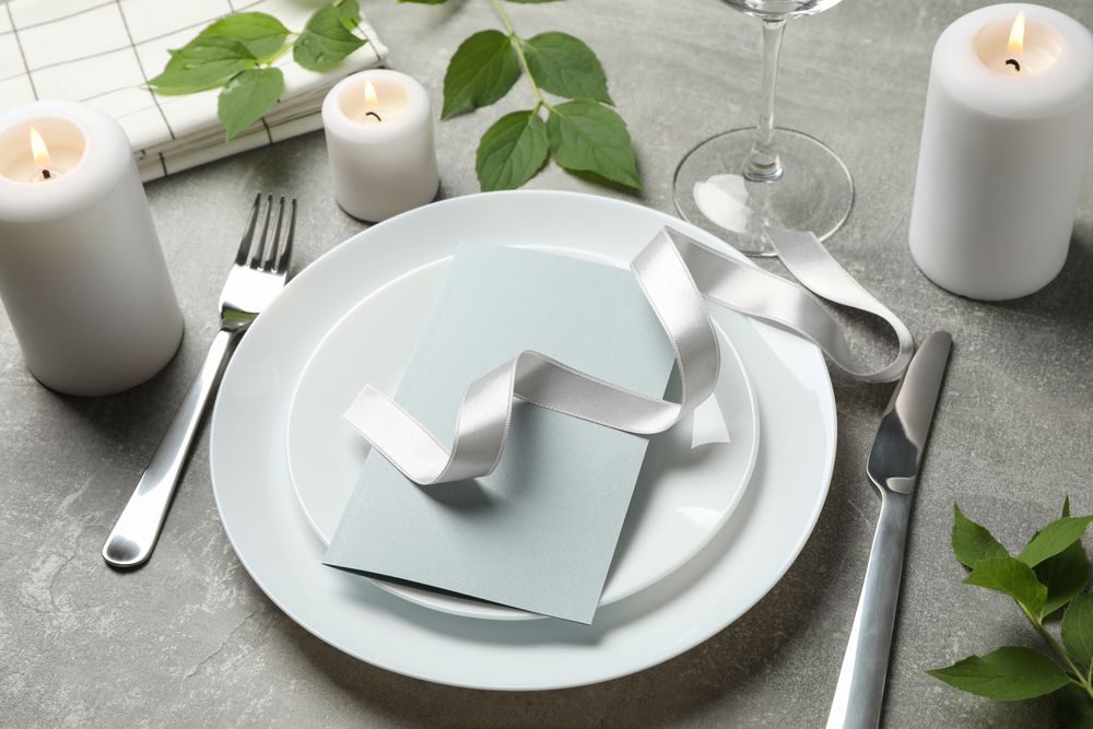 Composition of table setting with candles, leaves and cutlery on gray background