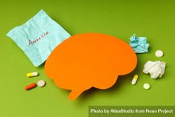 Orange paper cut out of brain on green background with pills and post it notes 0W3r60