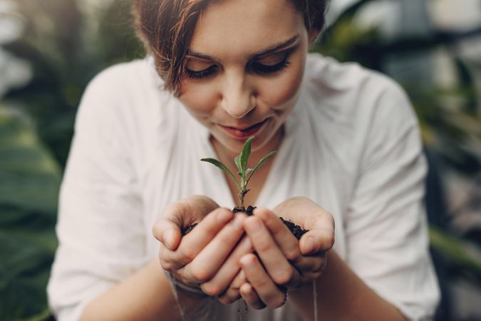 Beautiful young woman smelling small plant in garden center