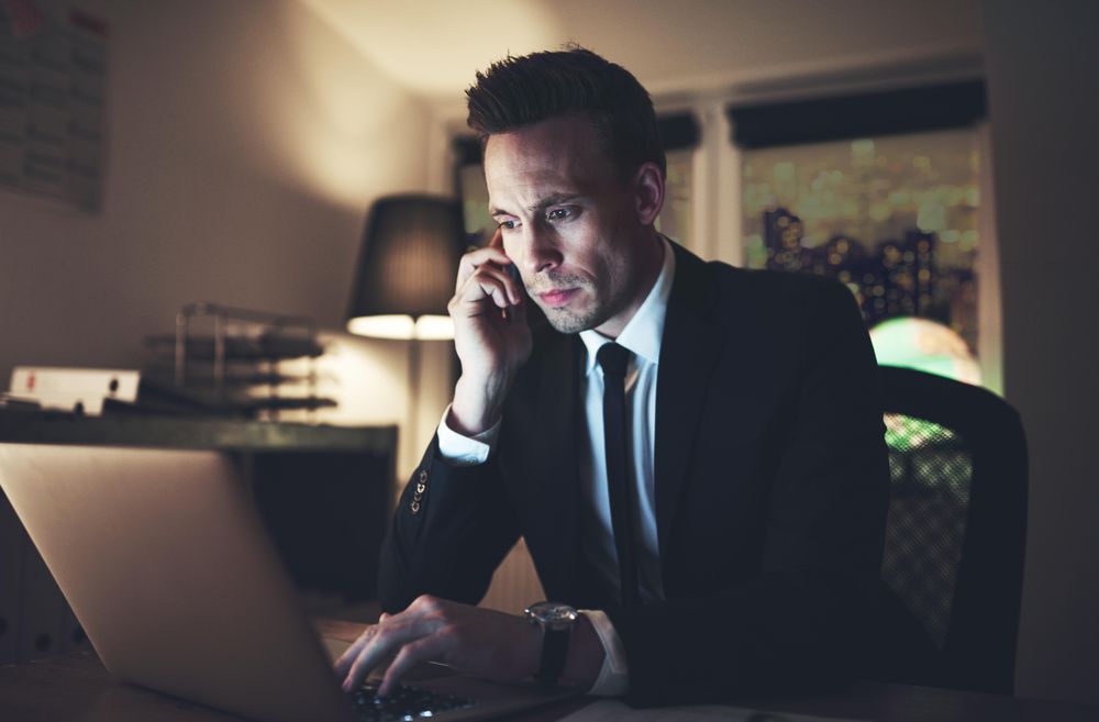 Business man on his cell phone at night while working on his laptop