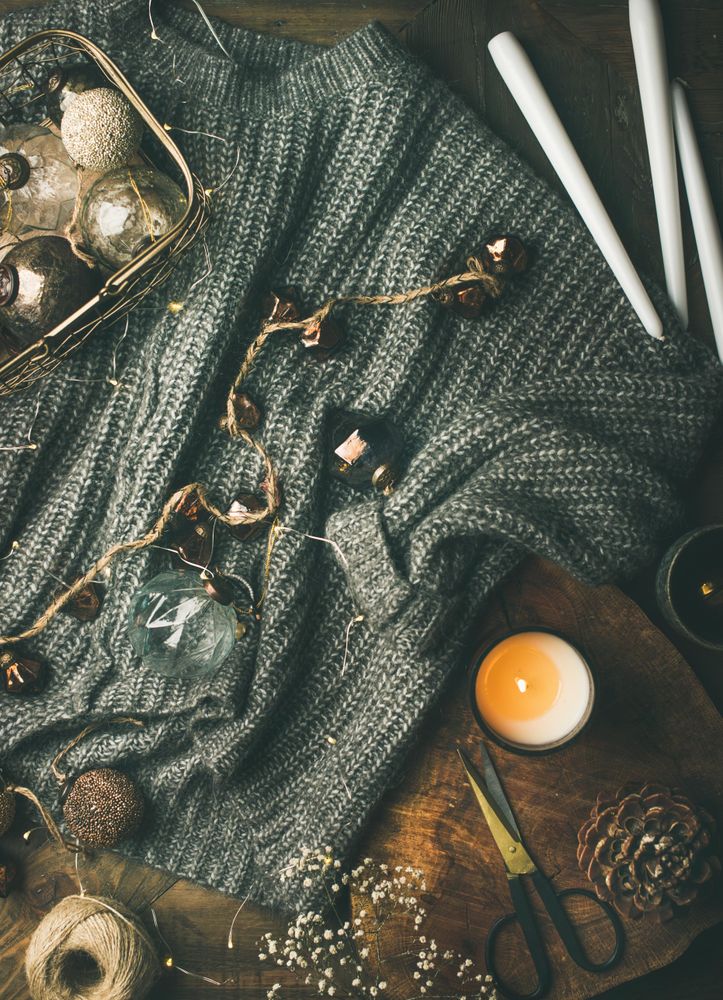 Festive decorations, candles and garland resting on grey woolen sweater