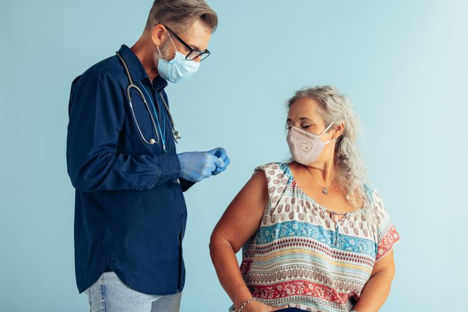 Male doctor preparing syringe for vaccinating woman against blue background