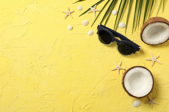 Starfishes, coconut, palm branch and sunglasses on yellow background, space for text