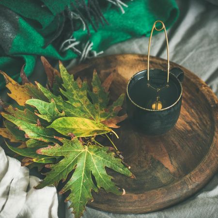 Fall leaves next to tea cup with infuser on wooden tray