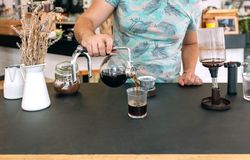 Unrecognizable barista pouring specialty coffee from Japanese siphon coffee maker into a glass