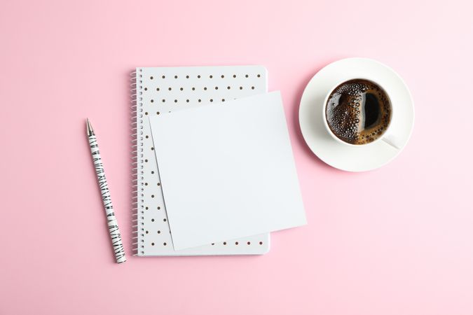 Cup of coffee with copybook and pen on color background, top view