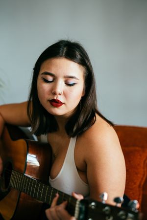 Young woman with red lipstick playing guitar with eyes closed