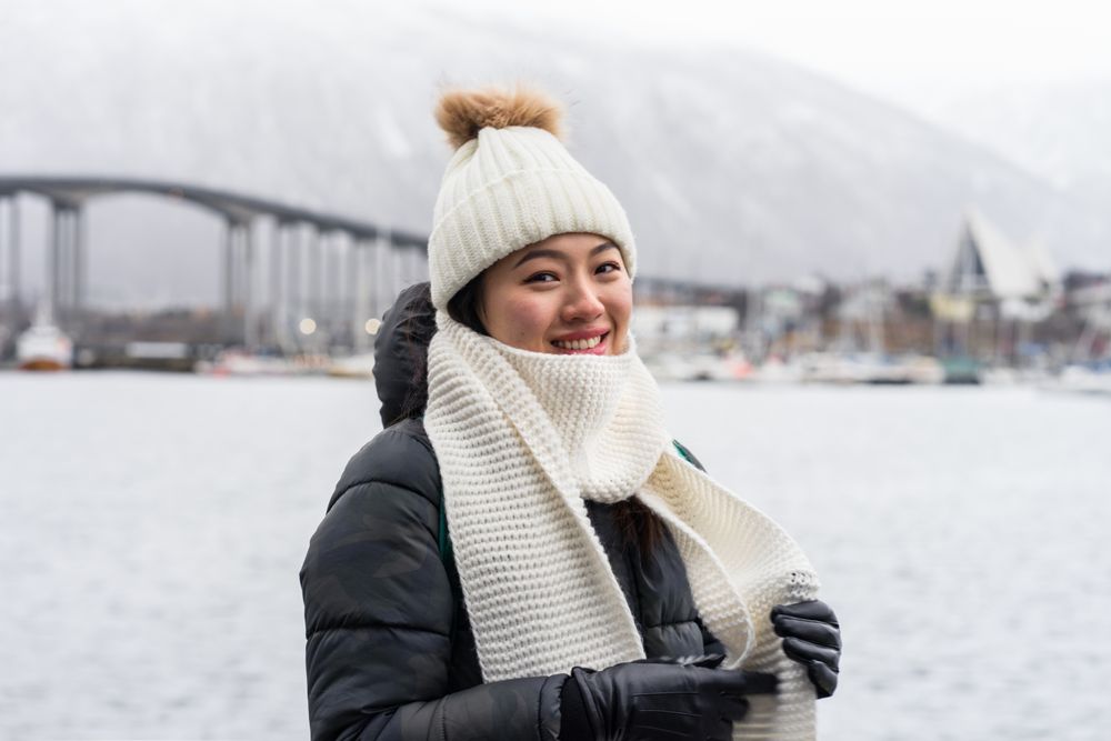 Asian female tourist in warm wear at snowy field near city