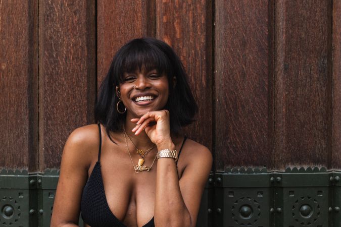 Cheerful Black woman in black outfit against wooden wall