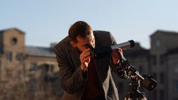 Man in grey coat carefully aligns telescope for solar observation