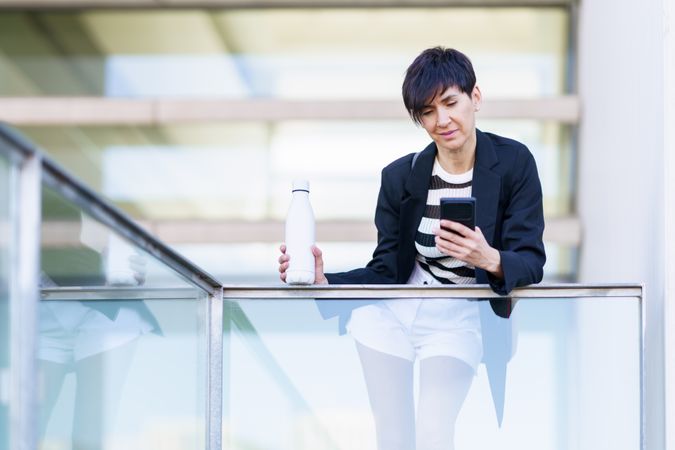 Woman taking break from work leaning outside of building with bottle