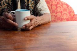 Hands of older person resting on table with mug of coffee
