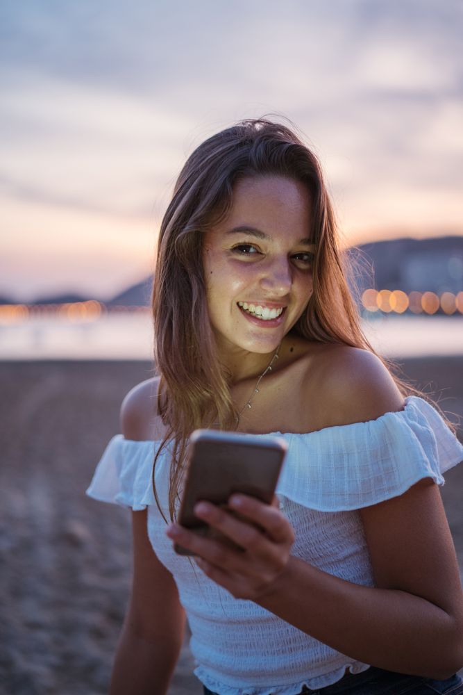 Cheerful young woman using smartphone on resort