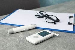 Blood glucose meter, glasses and paper tablet on gray table
