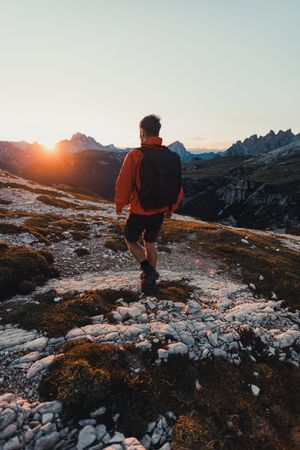 Back view of a man in red jacket with backpack hiking in mountains at sunset