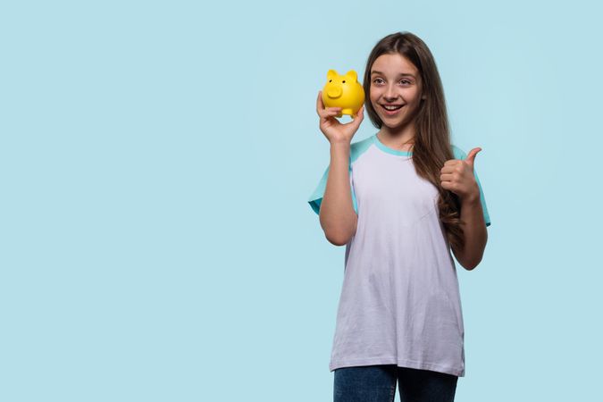 Girl gives thumbs up while holding yellow piggy bank