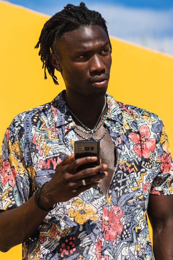 Stylish Black man in colorful shirt with smartphone
