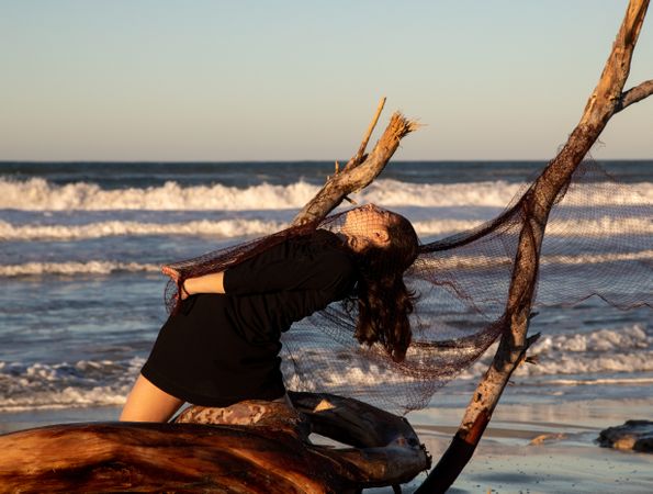 Woman in fishing net fixed on twig near water on shore