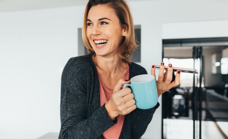 Smiling woman enjoying coffee while talking over phone at home