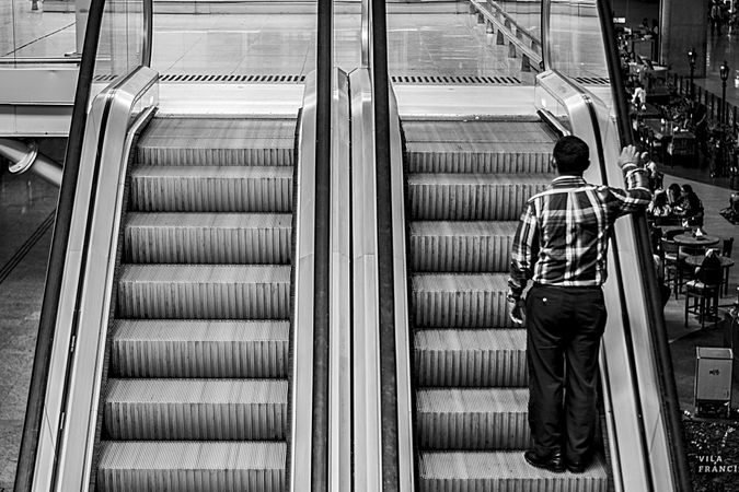 Back view of man standing on escalator in grayscale