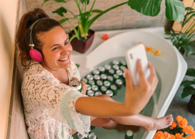Cheerful woman in bathtub taking selfie