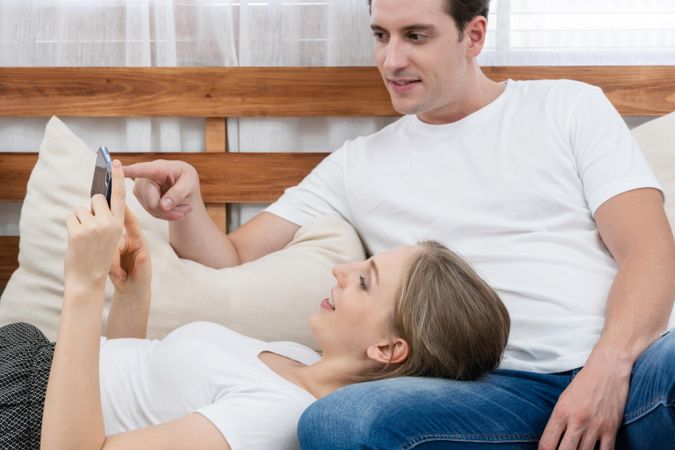 Woman lying on husband as they both read something on her phone