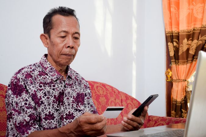 Asian male holds and looks at the blank credit card doing payment online