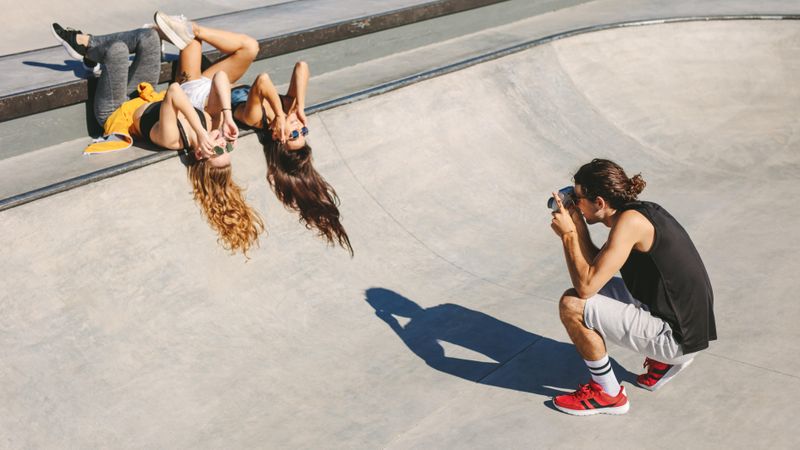 Male friend taking picture of female friends posing with sunglasses