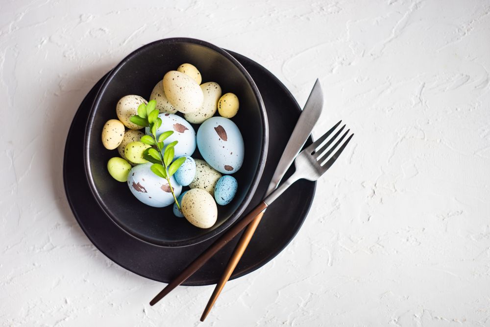 Easter table setting with colorful eggs of difference sizes in dark bowl