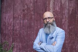 Front view of a mature trendy bearded hipster standing against a vintage red door outdoors while looking to camera