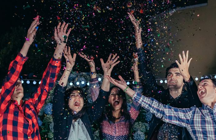 Group of friends celebrating at party and throwing confetti
