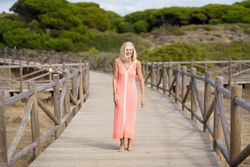Mature female with grey hair going for a stroll on wooden walkway near the coast