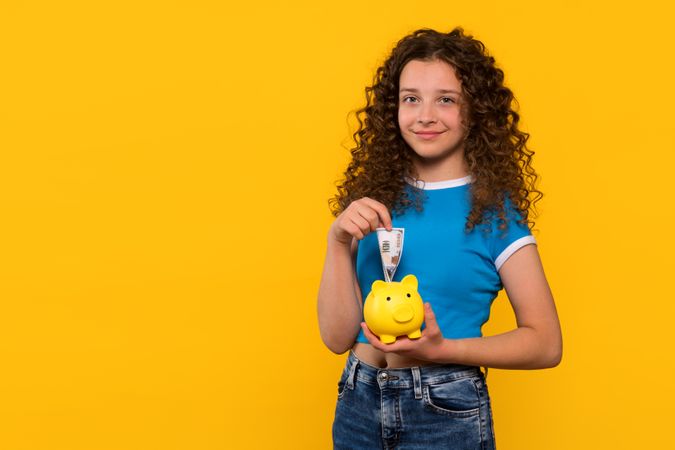 Smiling girl holding a piggy bank and saving money.