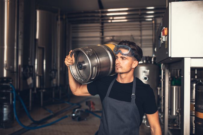Young white male wearing apron and goggles on head in keg storage room