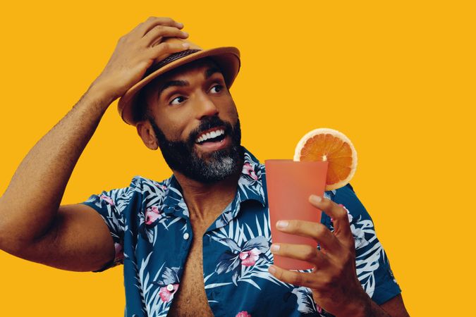 Surprised male wearing colorful shirt and looking away with cocktail with yellow background