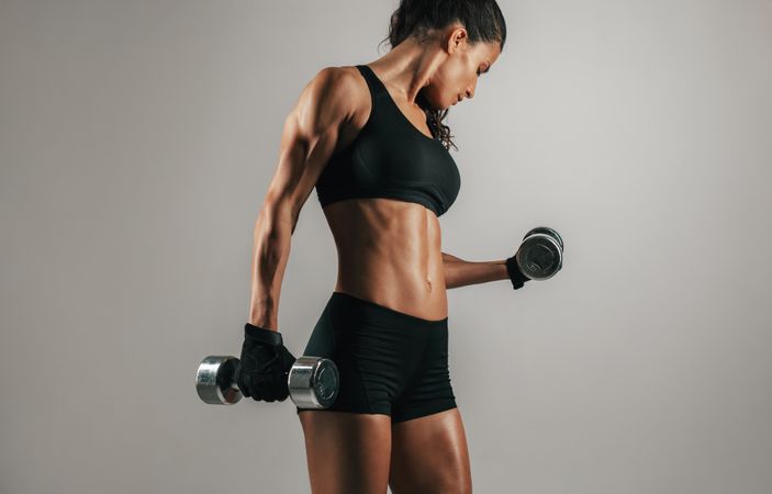 Strong woman lifting weights over gray background