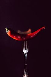 red chili pepper on fire in fork on a dark background
