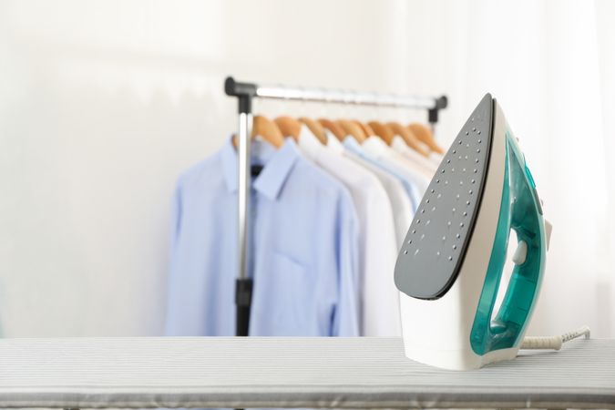 Iron on ironing board against light background, space for text