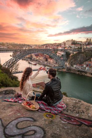 Woman and man having a picnic and having wine over the river by the two during sunset