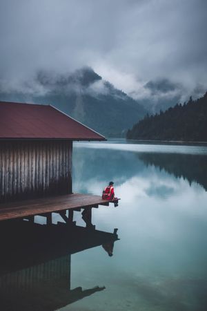 Person sitting on dock over lake under cloudy sky